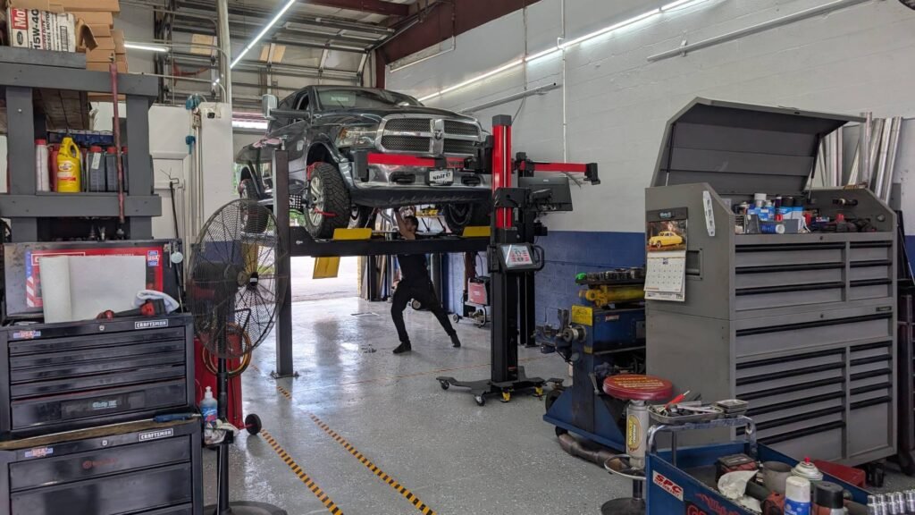 A High Tech Motors technician performs a precision wheel alignment on a silver sedan using Hunter Engineering equipment at a West Palm Beach, Florida auto repair shop